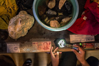 A Chinese trader inspects a rough jade stone, worth around 20-30 thousand USD, in a hotel room which serves as a black market jade trading centre.