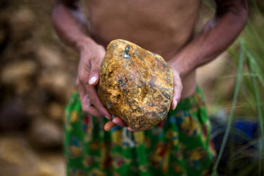 A miner holds a raw jade stone that he found in a mine. The weathered exterior often disguises a beautiful and valuable interior.