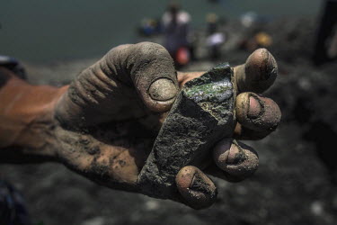 An informal jade miner holds a rough jade stone that he found among the waste debris from a commercial jade mine. To differentiate jade from an ordinary stone, the miners spits on the stone which they...