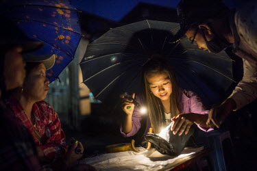 A Chinese trader, sheltering from the rain beneath an umbrella, inspects a jade stone by torch light a jade market in Hpakant.