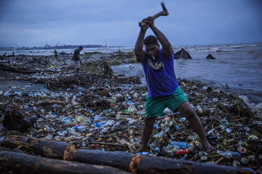 A man cuts up a log for firewood after it was washed onto the beach, along with large amounts of natural and man made debris, during floods . In February 2015, on Guadalcanal Island, tropical rains fe...