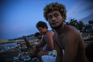 Piter Havae, 16, sits on a log that was carried, along with large amounts of man made debris, to the beach by a river during flooding. He says: 'It is very sad to see our home full of garbage. It happ...