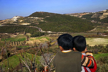 Two boys look across the border to Syria from a rooftop in Guvecci. Guvecci was once a central hub for smuggling of munitions and supplies to the Free Syrian Army. However, smuggling activities have b...