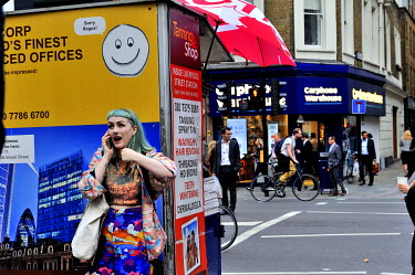 A woman with blue hair and Japanese inspired clothing talking on a mobile phone outside Liverpool Street Station.