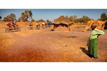 A woman looks towards a group of cyclists riding through her village during the Senegal Classic. Filip Meirhaeghe, Belgian mountain bike world champion in 2003, organises an annual mountain bike race...