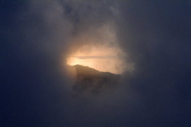 A gap appears in the clouds as the sun sets behind Sunset Peak on Lantau Island.