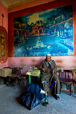 A man checks his mobile phone while smoking a shisha (sheesha, narghile, hookah) water pipe in a cafe.