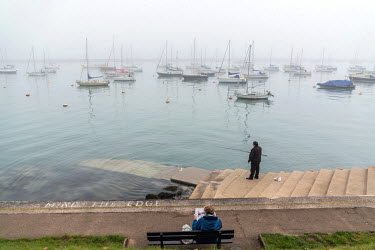 A man fishing in the early morning in Brixham harbour.