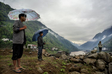 Villagers, sheltering from rain beneath umbrellas, look across the Nujiang River at a landslide that blocked the main road for two days.