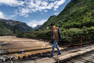 A youth speaks on a mobile phone while walking across the suspension bridge spanning the Nujiang River in Mian Gu village.