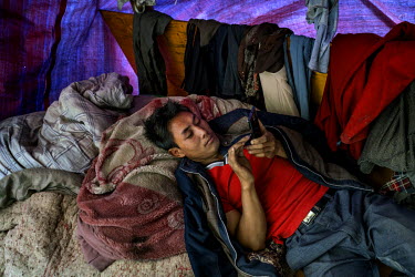 A construction worker uses his mobile phone while resting inside the shelter where he lives with his family close to the Nujiang River.