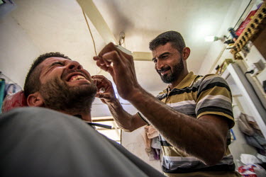 Rokam Hamoud cuts a customer's hair in his barber's shop that he reopened following the village's liberation from ISIS.