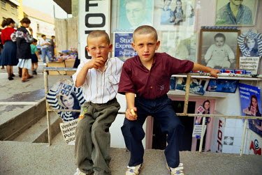 Two young boys with shaven heads sit on a fence on a shopping street in central Istanbul.