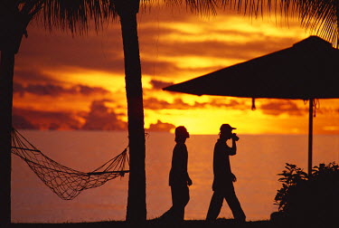Two men walk along a beach at sunset, beside the swimming pool of a luxury hotel, near the Tunku Abdul Rahman National Marine Park.