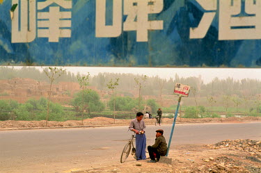 Two Uighur youths wait at an isolated bus-stop on the outskirts of Kashgar.