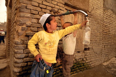 A young ethnic Uighur boy keeps his trousers from falling down while collecting water from a leaking faucet in the old city.