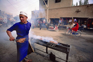 An ethnic Uighur cooking skewered mutton at a streetside restaurant.
