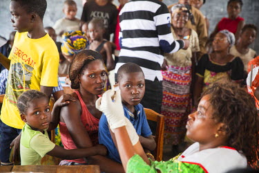 A mother and her children look on as a medical worker prepares an injection of yellow fever vaccination at a school in the Zone de Sante Kikimi.  Following an outbreak of mosquito-borne viral infectio...