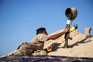 A fighter of the Al-Marsa Brigade, fighting IS in Sirte, holds up a helmet mounted on the barrel of his AK-47, to draw fire from nearby snipers on a frontline position near the sea front.   Various Li...