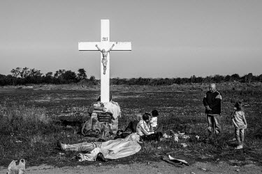 A group of refugees rests on the ground at the foot of a crucifix built to bless the local agriculture.