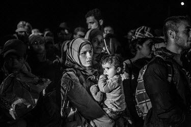 A woman holds a child as she stands among a group of refugees crowding onto one of the few available buses taking them to various destinations as they seek to travel onto Western Europe.