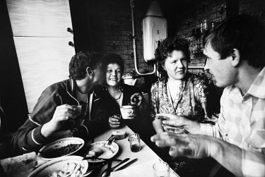 Two couples sitting in a kitchen drinking homemade vodka and eating.