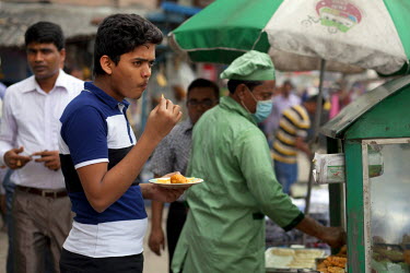 A customer eats fried snacks cooked and served from his mobile food cart by Zafar in the Nari Moitree district.