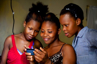 Djenise Hilaive (centre) and her daughters Edna (in red) and Sendie looking at pictures on a mobile phone.
