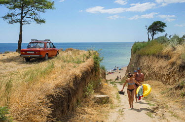 A Lada car parked over looking a Black Sea beach as a young family make their way from the seafront.