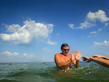 A man tries to protect himself from his wife's splashes as they play in the sea.