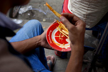 A customer of Ariful Islam Zafar eats chips from a plate. Zafar serves food from a food cart he was given by Concern in Nari Moitree, Paltan, Dhaka.