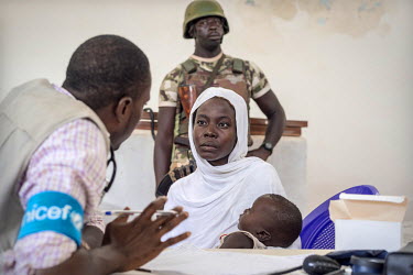 Dr Ernest Okoli (33) talks to a mother as he gives her sick child medication. Soldiers provide security in a territory where the surrounding hills are still occupied by the Islamist group Boko Haram....