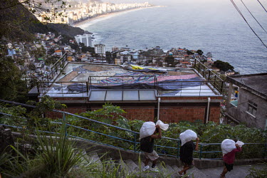 Three workers, carrying sacks, descend from the top of Vidigal, a favela with views of Rio's South Zone beaches.