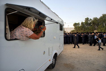 A traveller takes a photo, out of her caravan window, of Ultra-Orthodox Jewish men and boys praying during a 'Tashlich' ritual beside the Mediterranean Sea. 'Tashlich' ('to cast away') is a ritual whe...