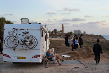 A holidaying couple enjoying the sun outside their caravan as Ultra-Orthodox Jews gather for a 'Tashlich' ritual beside the Mediterranean Sea. 'Tashlich' ('to cast away') is a ritual where believers g...