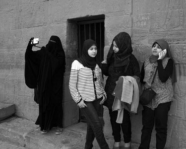 A group of girls and a woman, in a full veil taking pictures and selfies, visit the temple om the island of Philae in the Nile river.