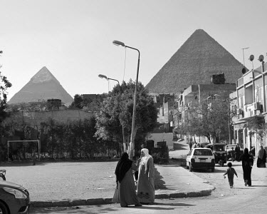 Two women talking on a street in Giza with the famous pyramids in the background.