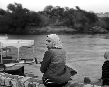 A woman sits on a wall beside the Nile, enjoying the sunset.