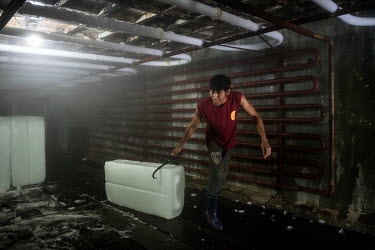 A worker drags a block of ice from the cold room of an ice factory that supplies the town's fishing boats.