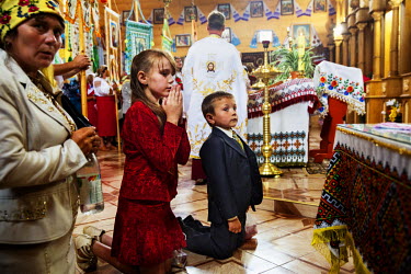 Children kneel at the altar for Communion in the Orthodox Church during the annual village celebration.