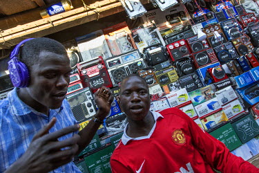 Young men listen to music in a market stall stuffed with radios and electronics.