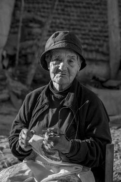 The aged Maria de Lurdes Branco sits in the open air in front of her home and works on her needle-lace.