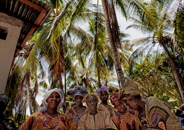 A group of women in traditional dresses stand under palm trees at a local celebration.