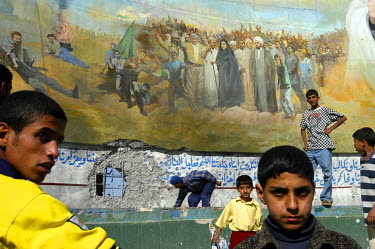 Children in front of a mural bearing a hole caused by a US tank shell in the poor Shiite neighbourhood of Sadr City.