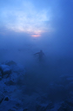 A man wades in a lake on a winter evening.