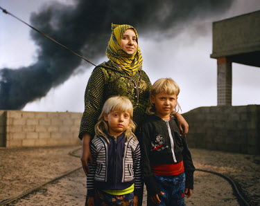 Fatima Mahmoud, 38, with her sons Ali and Mohammed (on the roof top of their house. ISIS set 19 of the town's oil wells on fire when they retreated a few months ago.  The fires have been burning ever...