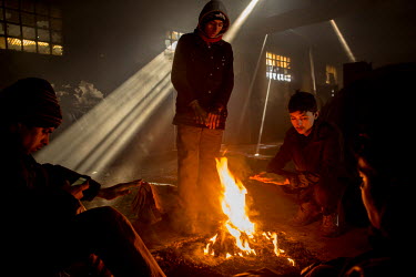 Afghani refugee Azrat Ali, 13, squats beside a fire trying to keep warm as temperatures outside fall to minus 15 Celsius. Ali is one of a group of migrants and refugees who are living in a squalid for...