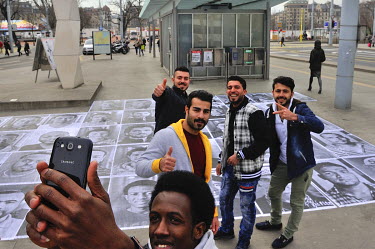 A group of young asylum seekers take a selfie after pasting portraits of refugees onto the ground at a busy intersection in the Plainpalais district of Geneva. The portraits are of people from various...