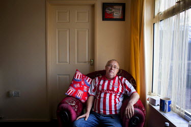 Leonard Bradbury (currently unemployed after suffering a workplace injury ) at his home on the Bentilee Estate. He is wearing a replica Stoke CIty FC shirt and rests on a Stoke City branded cushion.