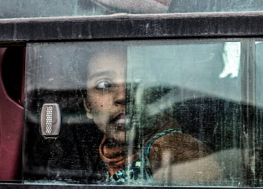 A girl, displaced by the fighting in Mosul between ISIS and advancing government forces, looks out of the window of the bus transporting her to a nearby IDP camp, while elsewhere the men of the family...